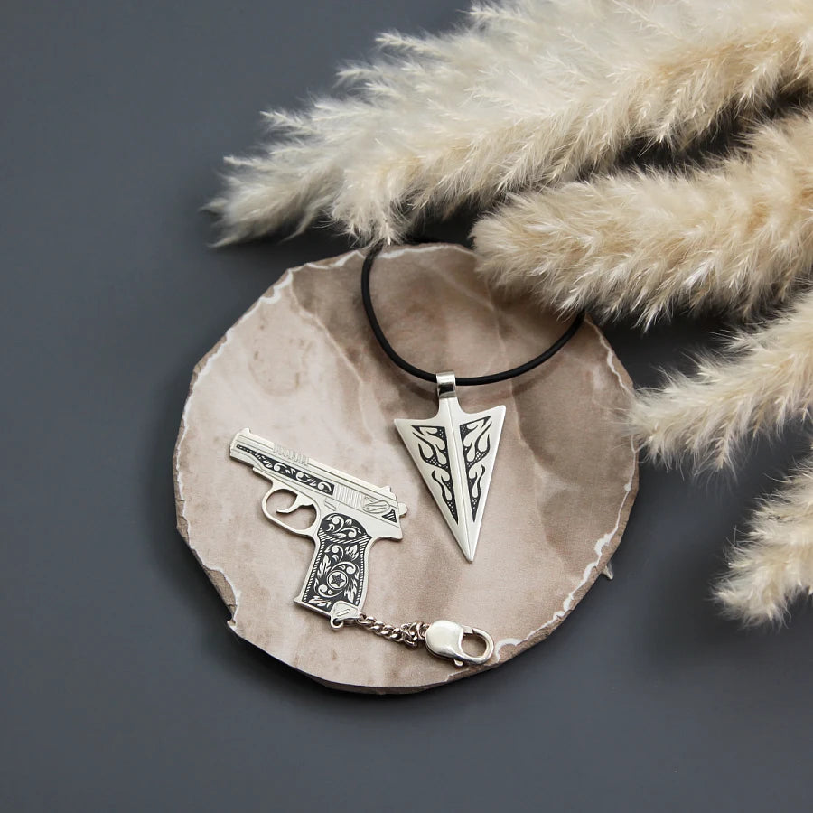Geschenkset Starker Charakter auf Holzschale — rustikale Inszenierung mit Pampasgras im Hintergrund, Pistole und Pfeilspitze als maskuline Talismane in 925 Silber