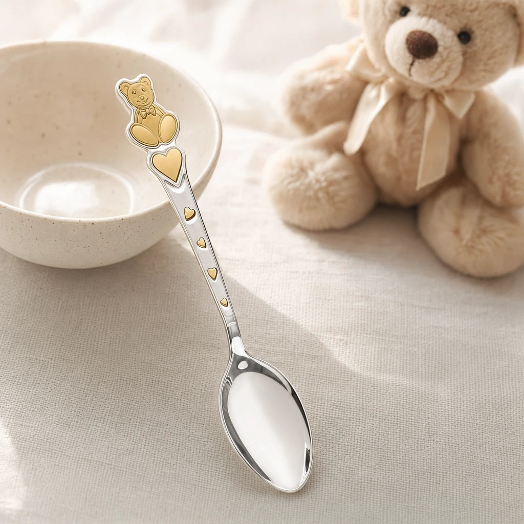 Kinderlöffel aus 925 Silber mit vergoldetem Teddybär und Herzen auf hellem Leinentisch neben einem Plüschbären — Lifestyle