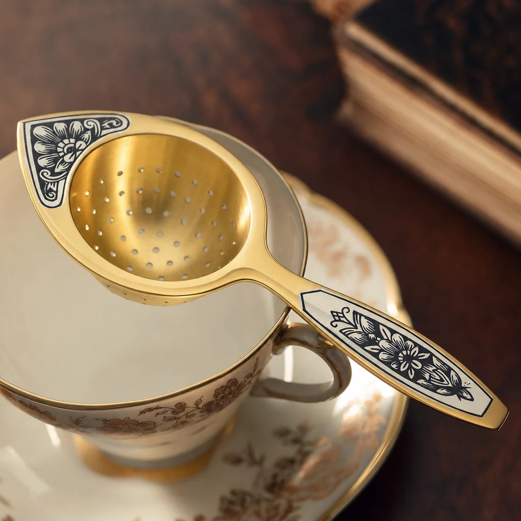 Teesieb Aurora Gold 925 Silber vergoldet quer über einer Porzellantasse — Niello-Ornament am Griff in Nahaufnahme, Lifestyle