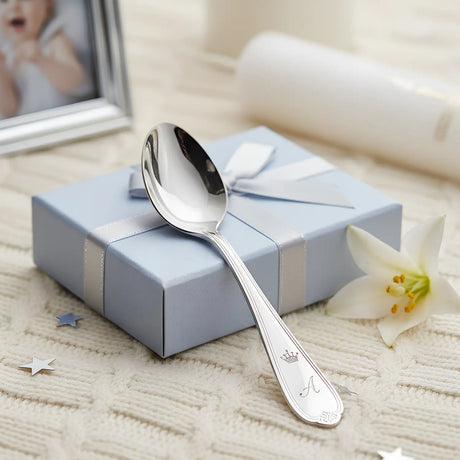 Eleganter Babylöffel aus 925 Sterling Silber mit Gravur, präsentiert auf einem weichen Stricktuch neben einer blauen Geschenkbox und einem Babyfoto.
