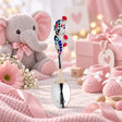 Babylöffel aus 925 Silber mit roter und blauer Emaille, fliegender Elefant — Lifestyle-Aufnahme in Rosa mit Plüsch-Elefant und Babyschuhen, Geschenk zur Geburt eines Mädchens
