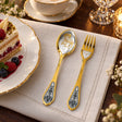 Dessertbesteck Sternzeichen Widder aus 925 Silber vergoldet neben einem Dessertteller mit Torte – vergoldetes Widder-Bild im Löffel, Symbol auf der Gabel