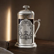 French Press aus 925 Sterling Silber mit Akanthus-Medaillon im warmen Abendlicht auf dunklem Nussholz — Lifestyle