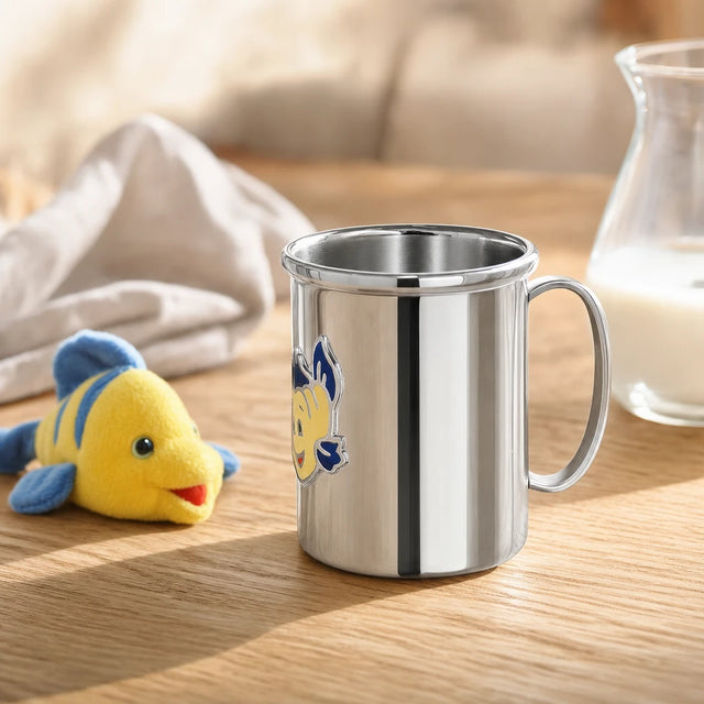 Kinderbecher aus 925 Silber mit gelb-blauem Fisch-Motiv auf einem Eichentisch am Frühstücksplatz — Lifestyle