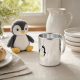 Kinderbecher aus 925 Silber mit Emaille-Pinguin auf gedecktem Frühstückstisch neben einem Plüsch-Pinguin — Lifestyle