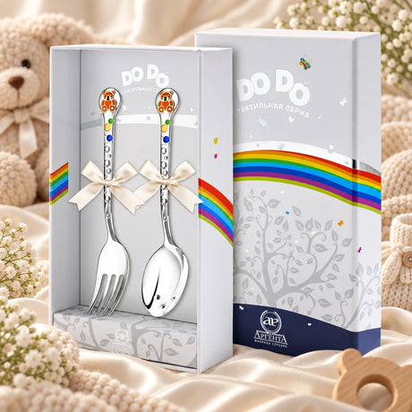 Kinderbesteck Teddybär 925 Silber — Emaille orange-gold 2-tlg in der Original-Geschenkbox — Lifestyle-Aufnahme auf cremefarbenem Satin mit Plüschtier und Schleierkraut, Geschenk zur Geburt
