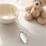 Kinderlöffel aus 925 Silber mit vergoldetem Teddybär und Herzen auf hellem Leinentisch neben einem Plüschbären — Lifestyle
