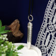Patrone als Silberanhänger an schwarzem Band — Psalm 91 rundum auf der Hülse, Geschenk für Jäger, vor blauem Stoff und Spitze