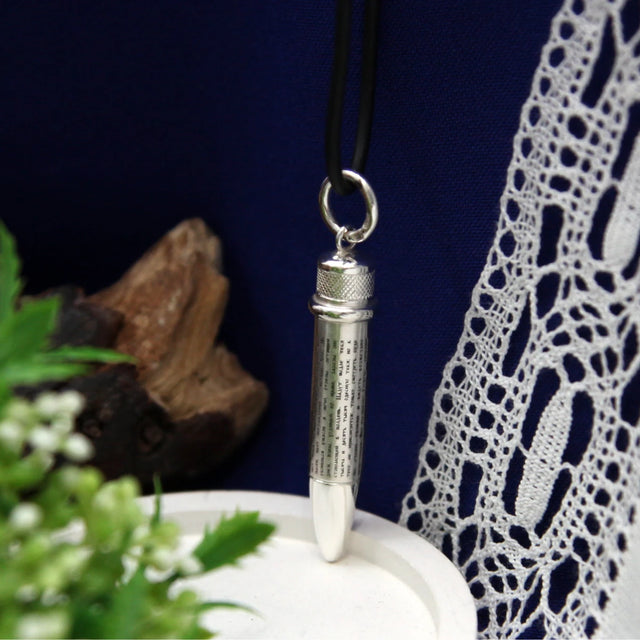 Patrone als Silberanhänger an schwarzem Band — Psalm 91 rundum auf der Hülse, Geschenk für Jäger, vor blauem Stoff und Spitze