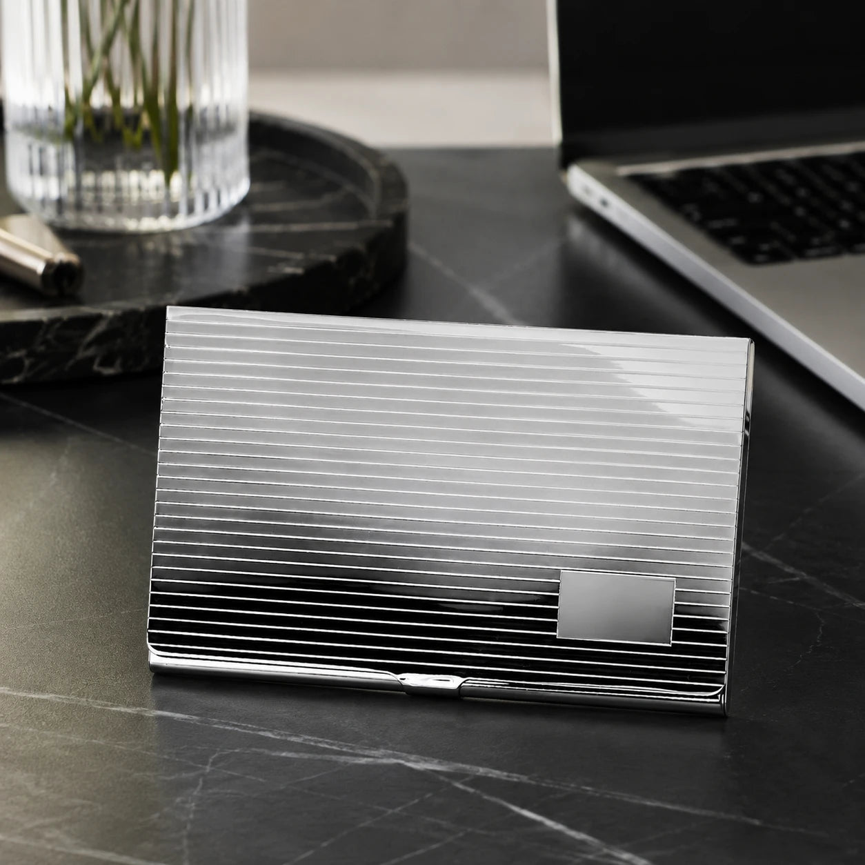 Visitenkartenetui Linea 925 Silber ArgentA — Lifestyle-Aufnahme auf dunklem Marmor-Schreibtisch mit Laptop, Stift und Vase im Hintergrund, Premium-Business-Setting